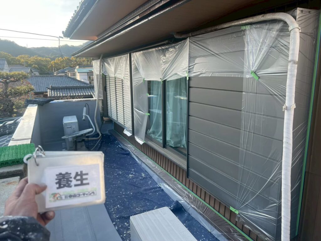 窓やサッシまわりを養生シートで覆い、塗装作業に備えて周囲を保護しています