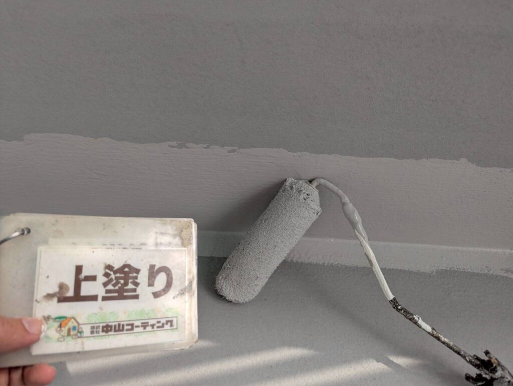 上塗りを施工しています。ローラーを使用して塗料を均一に塗り広げ、塗りムラや塗り残しがないよう丁寧に仕上げています