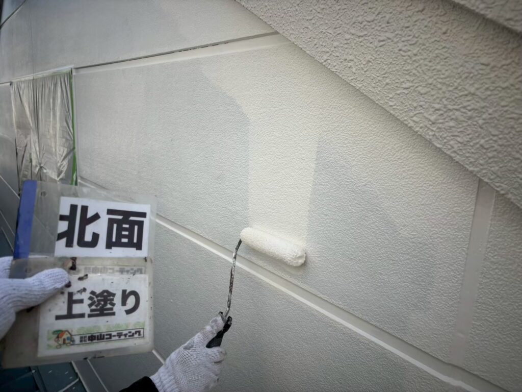 中塗り後の外壁に仕上げの上塗りを行っています