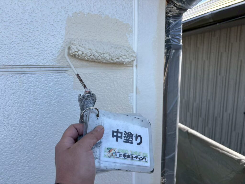 ローラーを使用して外壁の中塗りを行っています