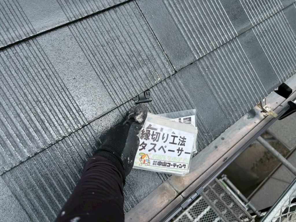 スレート屋根材の重なり部分にタスペーサーを挿入しています。屋根材同士の適切な隙間を確保し、雨水の排出経路を確保するための工程です