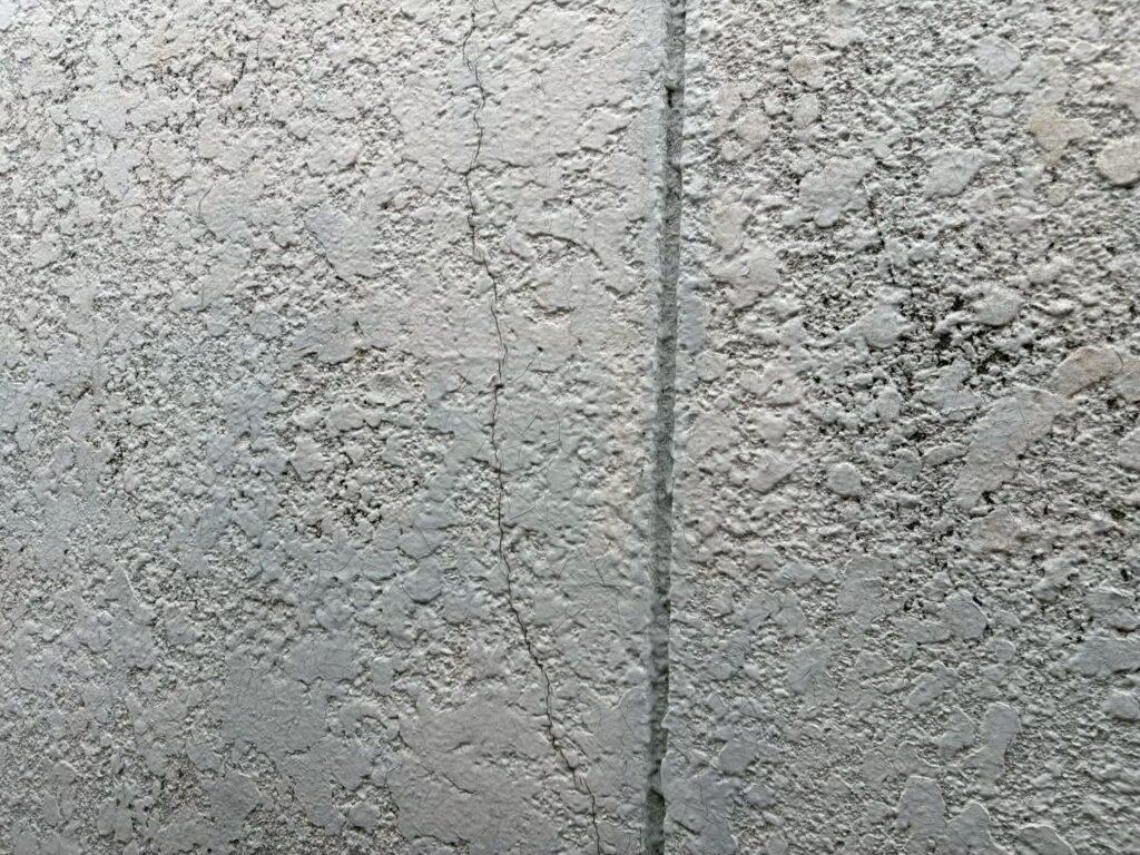 外壁には縦方向に伸びるクラックと、塗膜の細かなひび割れが見られます