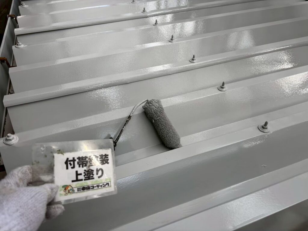 錆止め・中塗りを経た折板屋根に、仕上げとなる上塗りを行っています