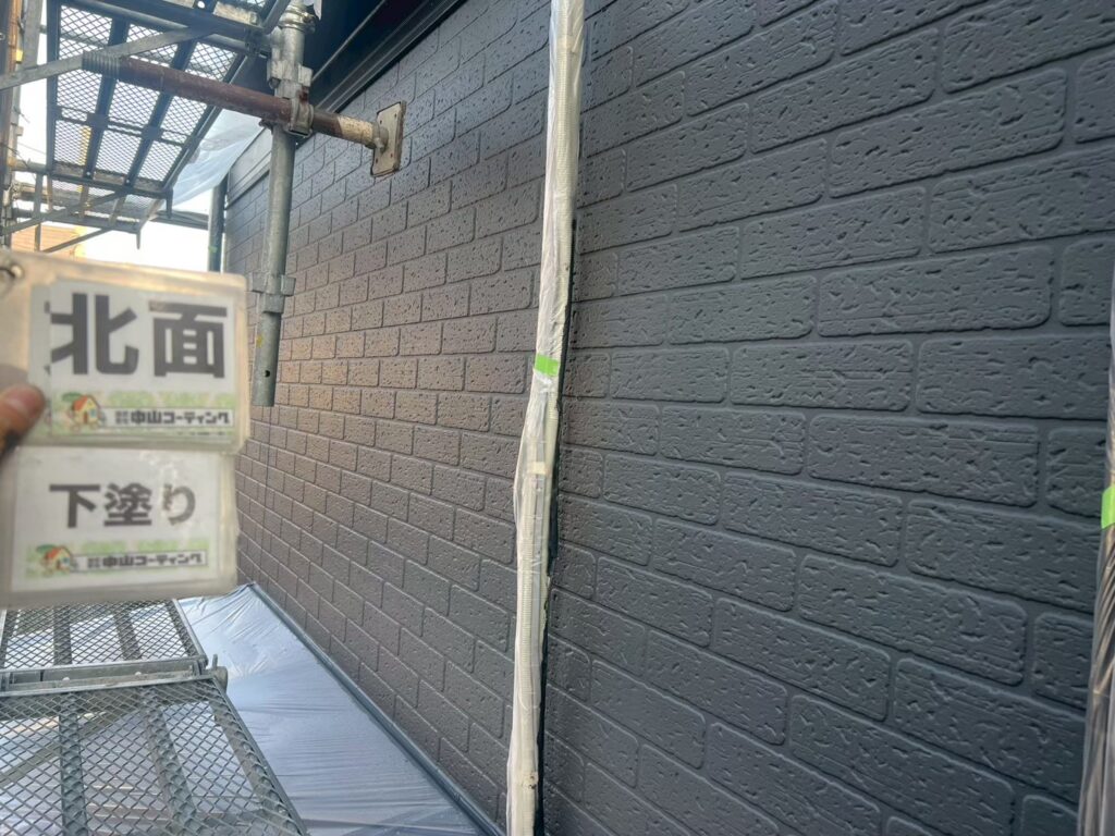 建物北面の外壁に下塗りを施した状態です。レンガ調サイディングの細かな凹凸や目地部分まで丁寧に塗装し、塗りムラのない均一な下地に整えています