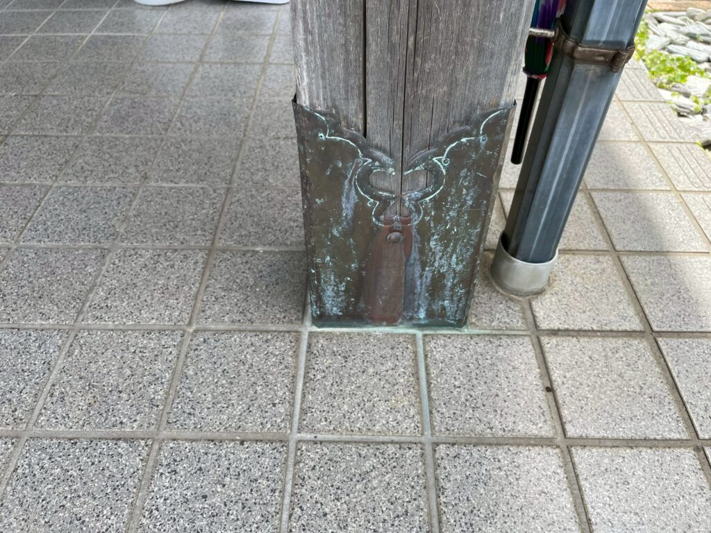 玄関柱の根元には金属製の装飾金物が取り付けられており、表面に緑青（ろくしょう・サビ）が見られます