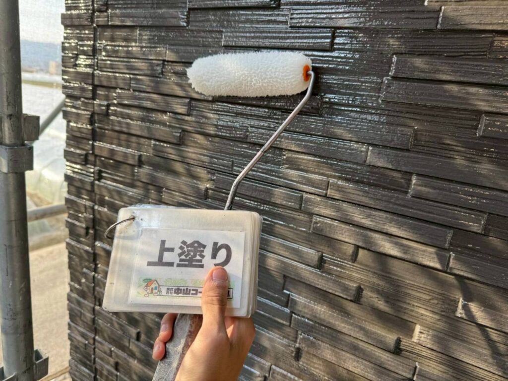 黒い外壁の凹凸に沿って、塗料をムラなく塗り広げます