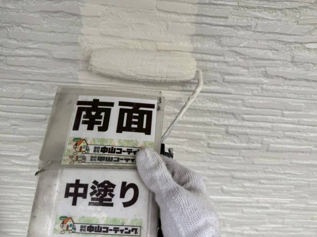 白い外壁の凹凸に合わせて、中塗り塗料を丁寧に塗布しています
